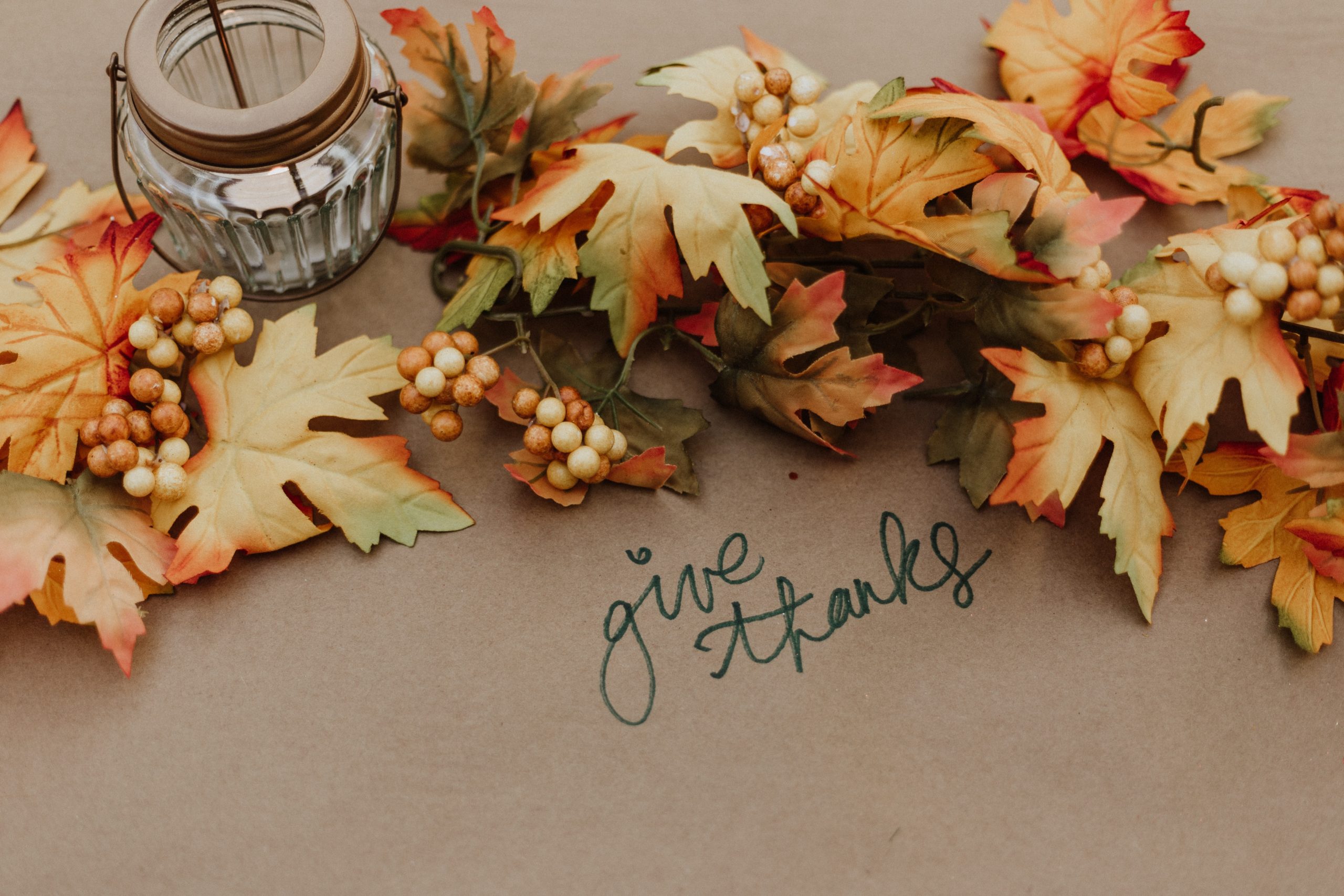 Image of Autumn leaves with berries, a candle and the words give thanks